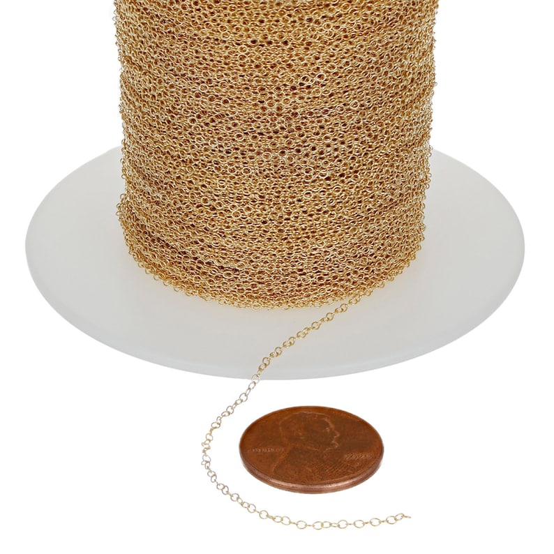 May include: A spool of gold chain with a section of the chain laying next to it. A penny is next to the chain for size comparison.