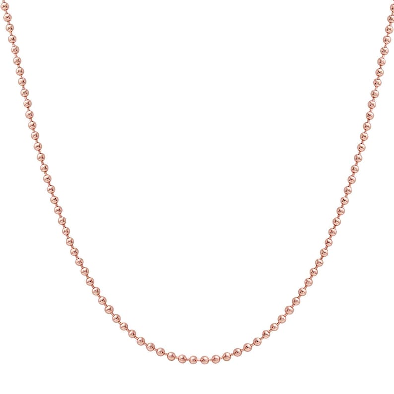 May include: A delicate rose gold ball chain necklace. The necklace is composed of small, evenly spaced, spherical beads. The chain is displayed against a white background, highlighting its color and design. This necklace is a simple yet elegant piece of jewelry.