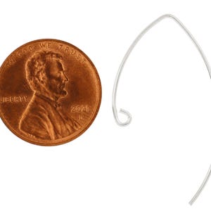 May include: A silver earring hook, shown next to a US penny for size comparison. The hook is a simple, curved shape with a small loop at the top.