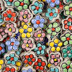 Könnte beinhalten: Nahaufnahme einer Sammlung von keramikblumenförmigen Knöpfen. Jeder Knopf hat eine weiße Basis und ein farbenfrohes Blumendesign in Rot, Blau, Gelb, Rosa und Grün. Diese Knöpfe sind wahrscheinlich für Möbel oder Dekorationszwecke bestimmt.