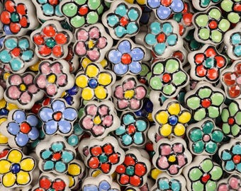 May include: A collection of ceramic flower-shaped knobs in various colors. Each knob features a white base with a colorful flower design in shades of red, blue, yellow, pink, and green. The knobs are likely for furniture or decorative use.