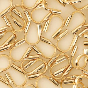 Op de afbeelding: Een close-up van een groep gouden metalen crimp kralen. De kralen zijn klein en hebben een afgeronde vorm. Ze worden gebruikt voor het maken van sieraden.