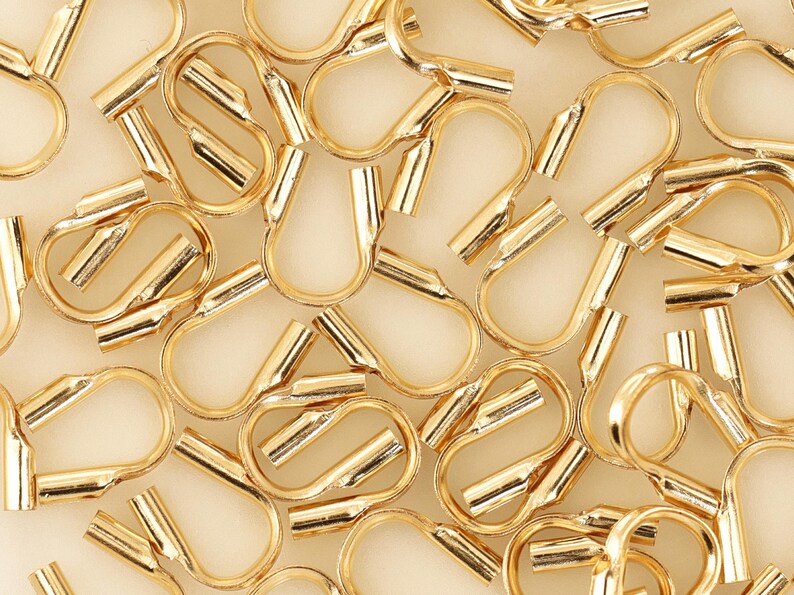 Op de afbeelding: Een close-up van een groep gouden metalen crimp kralen. De kralen zijn klein en hebben een afgeronde vorm. Ze worden gebruikt voor het maken van sieraden.