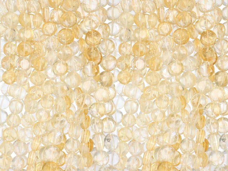 May include: Close-up of a collection of faceted, translucent beads in shades of yellow and clear. The beads are strung together, creating a textured, layered effect. Ideal for jewelry making or craft projects.