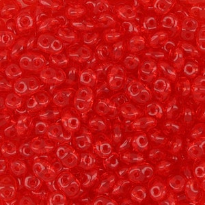 May include: A close-up shot of a pile of transparent, bright red beads. Each bead has two holes, giving them a unique shape. The beads are scattered, filling the frame and creating a textured surface.