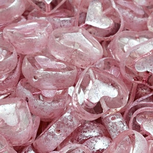 May include: A pile of pink heart-shaped glass beads with a silver shimmer. The beads are translucent and have a slightly frosted appearance.