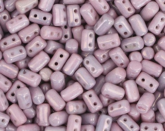 May include: A close-up of a pile of small, light purple glass beads with two holes in each bead. The beads have a slightly iridescent finish.