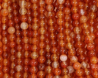 May include: A strand of orange carnelian beads. The beads are round and smooth, with a translucent finish.