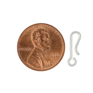 K&ouml;nnte beinhalten: Ein silberfarbener Metallhaken, etwa so gro&szlig; wie ein Cent-St&uuml;ck. Der Haken besteht aus Draht und hat eine einfache, abgerundete Form.