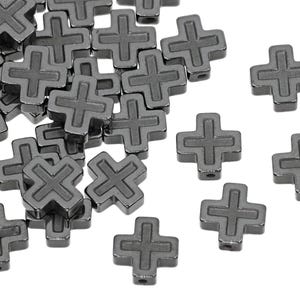 May include: A pile of black metal cross-shaped beads. The beads have a raised design and are scattered on a white background.
