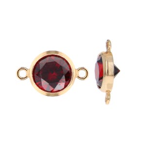 May include: Two gold-colored bezel set connectors with a round, faceted, deep red gemstone. Each connector has a loop on either side for attaching to other jewelry components. One connector is shown from the side.