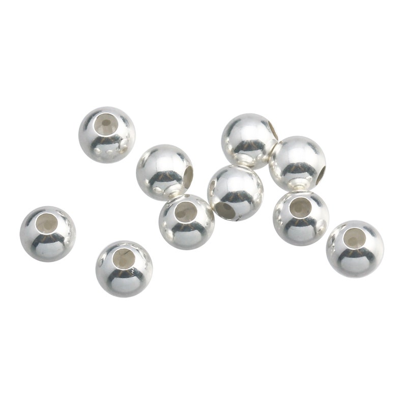 May include: A group of silver-toned round beads with a hole in the center. The beads are scattered on a white background.
