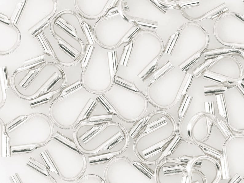 Op de afbeelding: Close-up van talrijke zilverkleurige krimpeindstukken, essentieel voor het maken van sieraden en knutselen. Deze kleine metalen componenten zijn ontworpen om de uiteinden van koorden of kettingen te bevestigen, wat een professionele afwerking geeft. Witte achtergrond.
