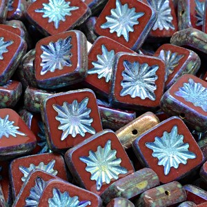 May include: A pile of square glass beads with a red and iridescent blue finish. Each bead has a raised starburst design in the center.