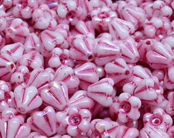 Puede incluir: Primer plano de un montón de cuentas de vidrio rosa con un diseño en forma de flor. Las cuentas tienen una base blanca con acentos rosas y un acabado brillante.