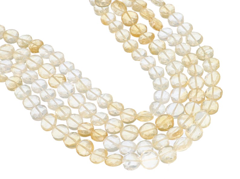 May include: Close-up of multiple strands of faceted, round gemstones in shades of yellow and clear. The beads are strung together, creating a layered effect. The gemstones have a polished, reflective surface, and are set against a white background.