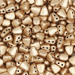 May include: A close-up view of a pile of small, triangular beads. The beads are a metallic gold color and have a matte finish.