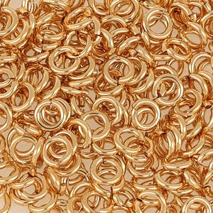 May include: A close-up image of a large pile of gold jump rings. The rings are all the same size and are arranged in a random pattern.