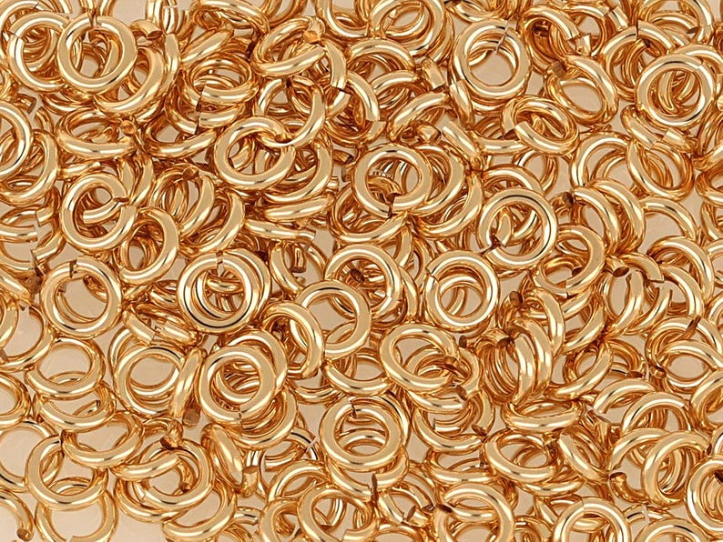 May include: A close-up image of a large pile of gold jump rings. The rings are all the same size and are arranged in a random pattern.