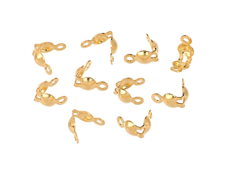 May include: A collection of gold-colored crimp end findings, designed for jewelry making. These small, curved metal pieces have a loop on one end and a curved shape to secure the ends of cords or chains. They are scattered on a white background.