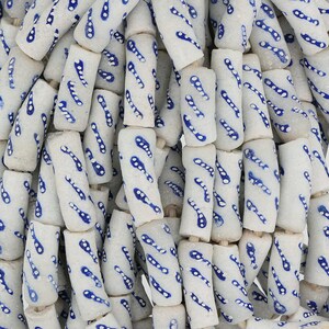 May include: A collection of white ceramic beads with a blue and white pattern. The beads are cylindrical and have a speckled texture.
