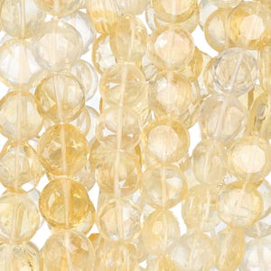 May include: Close-up of strands of faceted, round citrine gemstone beads. The beads are a mix of pale yellow and clear, with a sparkling, polished finish. The beads are strung together, creating a textured and visually appealing display.