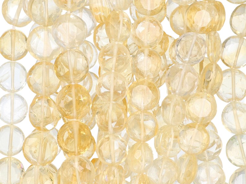 May include: Close-up of strands of faceted, round citrine gemstone beads. The beads are a mix of pale yellow and clear, with a sparkling, polished finish. The beads are strung together, creating a textured and visually appealing display.