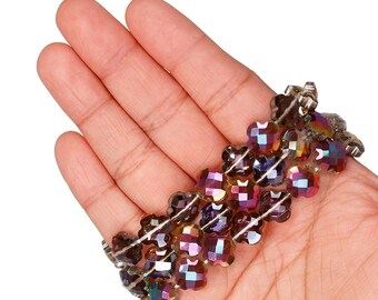 May include: A multi-coloured beaded bracelet with a floral design. The bracelet is made of faceted beads in shades of purple, gold, and iridescent colours. The beads are strung together on a clear elastic band. The bracelet is approximately 18 cm in length.