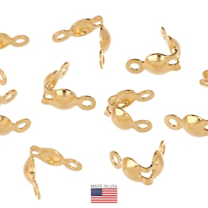 Peut inclure: Plusieurs éléments de bijouterie dorés, dont plusieurs pièces incurvées à extrémité ouverte avec de petites boucles. Les pièces sont dispersées sur un fond blanc. L'image comprend un petit drapeau américain.