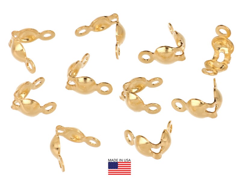 May include: A collection of gold-colored jewelry findings, including several open-ended, curved pieces with small loops. The pieces are scattered across a white background. The image includes a small American flag.