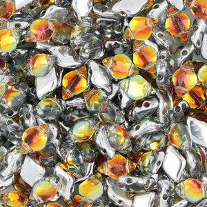 May include: A close-up of a pile of iridescent glass beads in shades of silver and orange. The beads are shaped like teardrops and have a faceted surface.