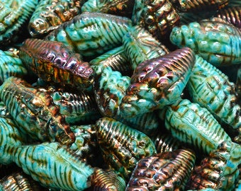 May include: A close-up of iridescent teal glass beads with a textured, shell-like design. The beads have a metallic sheen and are perfect for jewelry making or crafting.