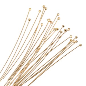 May include: A bundle of gold-colored head pins with round heads. The pins are arranged in a fan shape.