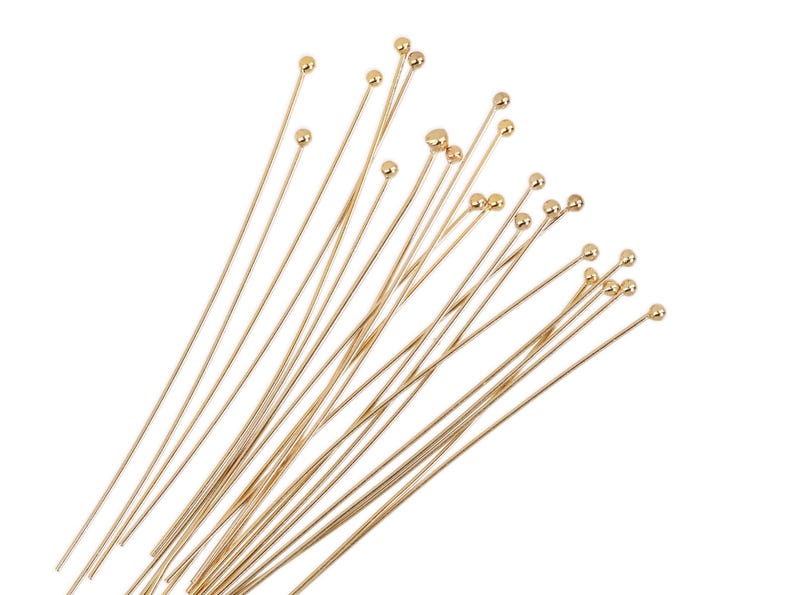 May include: A bundle of gold-colored head pins with round heads. The pins are arranged in a fan shape.