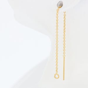 May include: A pair of gold chain earrings with a long, dangling chain on one side and a thin, straight bar on the other.