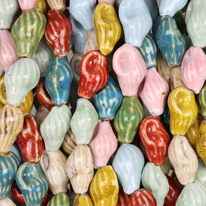 May include: A collection of colorful, ceramic shell-shaped beads in various shades of pink, green, yellow, blue, and red. The beads have a glossy finish and are arranged closely together, creating a textured surface.