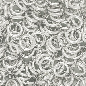 May include: A close-up of a pile of silver jump rings. The rings are all the same size and are arranged in a random pattern.
