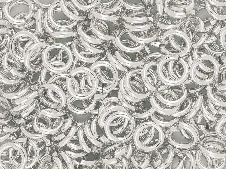 May include: A close-up of a pile of silver jump rings. The rings are all the same size and are arranged in a random pattern.