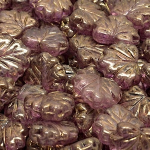 May include: A close-up of a pile of iridescent glass leaf-shaped beads. The beads are a light purple color with a gold metallic sheen.