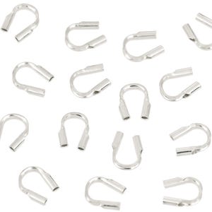Op de afbeelding: Een verzameling zilverkleurige krimpeindstukken, essentieel voor het maken van sieraden. Deze U-vormige componenten hebben twee open buizen voor het vastzetten van koorden of draden. De eindstukken zijn verspreid tegen een witte achtergrond.
