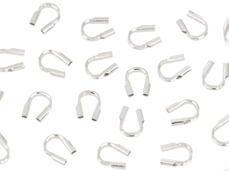 Op de afbeelding: Een verzameling zilverkleurige krimpeindstukken, essentieel voor het maken van sieraden. Deze U-vormige componenten hebben twee open buizen voor het vastzetten van koorden of draden. De eindstukken zijn verspreid tegen een witte achtergrond.