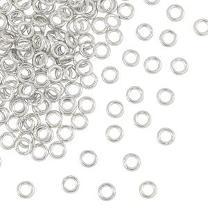 May include: A large pile of silver jump rings, with a few scattered on a white background. The jump rings are small and round, and they are ideal for jewellery making.