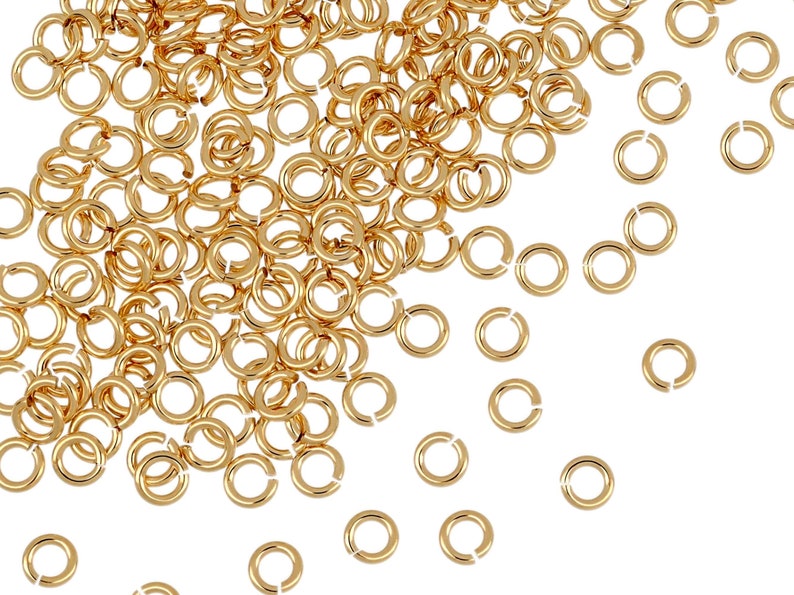 May include: A large pile of gold jump rings, with a few scattered around on a white background.