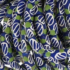 May include: A close-up of a strand of blue and white glass beads with green accents. The beads are cylindrical and have a pattern of white lines and green dots on a blue background.