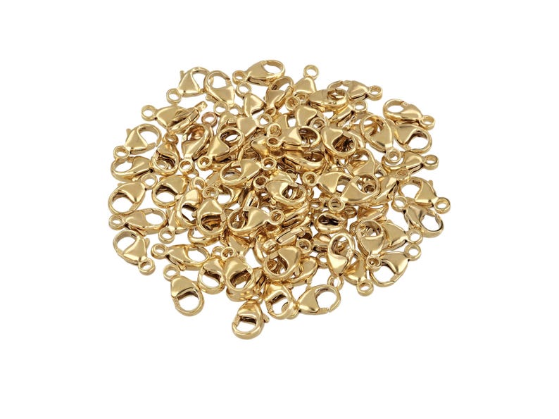May include: A large pile of gold-toned lobster clasps, a type of jewelry finding used for making necklaces, bracelets, and other jewelry.