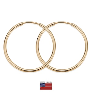 May include: A pair of gold-colored hoop earrings. The earrings are circular and have a smooth, polished finish. The image includes a small American flag with the text "MADE IN USA".