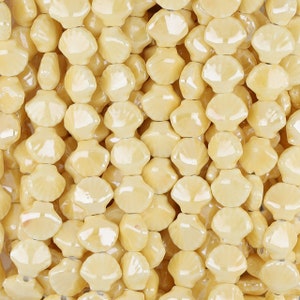 May include: A close-up of a strand of yellow glass beads. The beads are shaped like a flower with five petals. The beads are glossy and have a slight iridescent sheen.