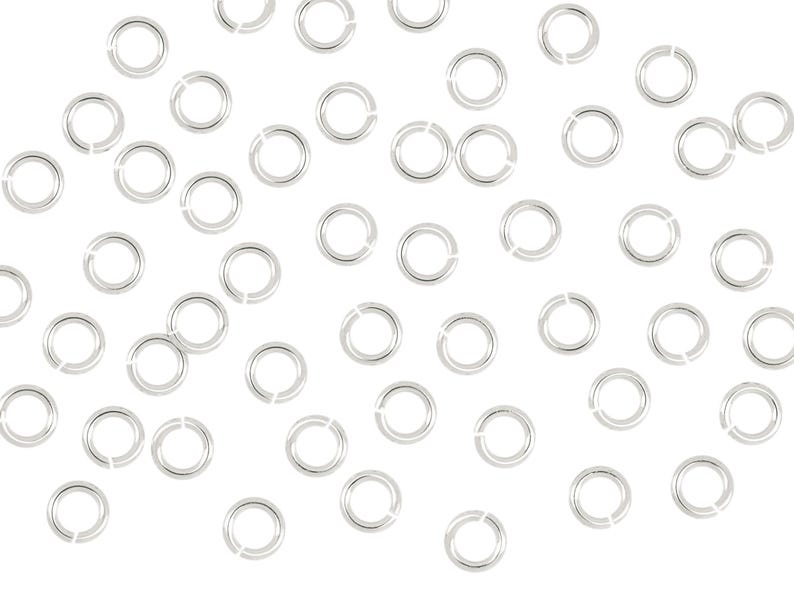 May include: A large quantity of silver jump rings, a type of jewelry finding, scattered on a white background.