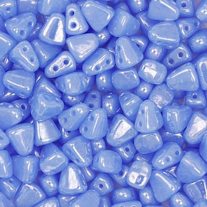 May include: A close-up of a pile of light blue iridescent glass beads. The beads are shaped like triangles with two holes in each bead.