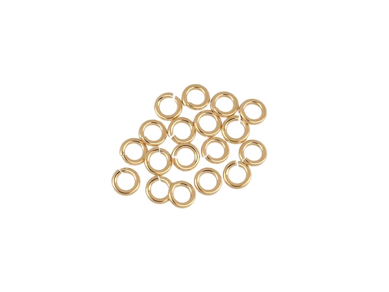 May include: A group of 20 gold jump rings, a type of jewelry finding, are scattered on a white background.